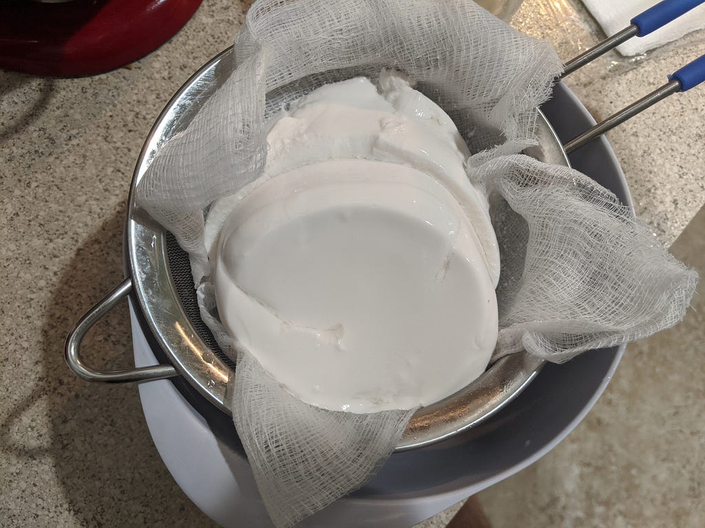 Fresh coconut yogurt being strained in a cheesecloth lined mesh strainer
