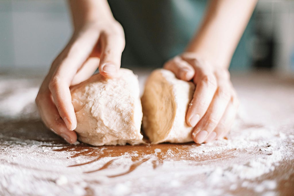 Hands kneading dough, symbolizing the human touch and craftsmanship essential for designing brands with wholeness and soul, going beyond mechanistic customer experience systems.
