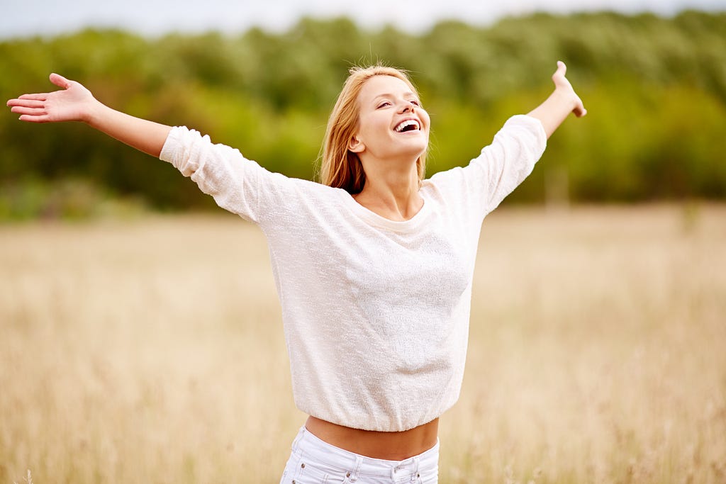 happy woman smiling with her eyes closed in a field with her arms outstretched.