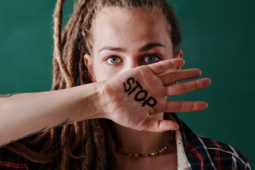 women lookin at camera, with her hand in front of her face, the word STOP is written on the palm of her hand.