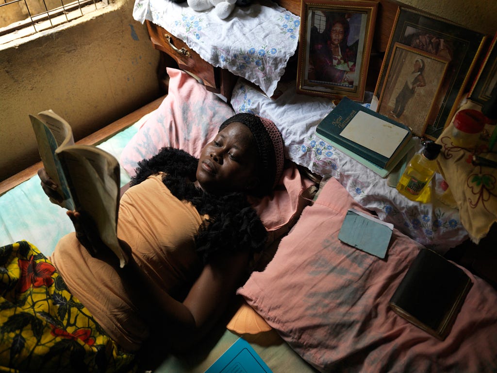 A young girl in Sierra Leone studies on her bed.