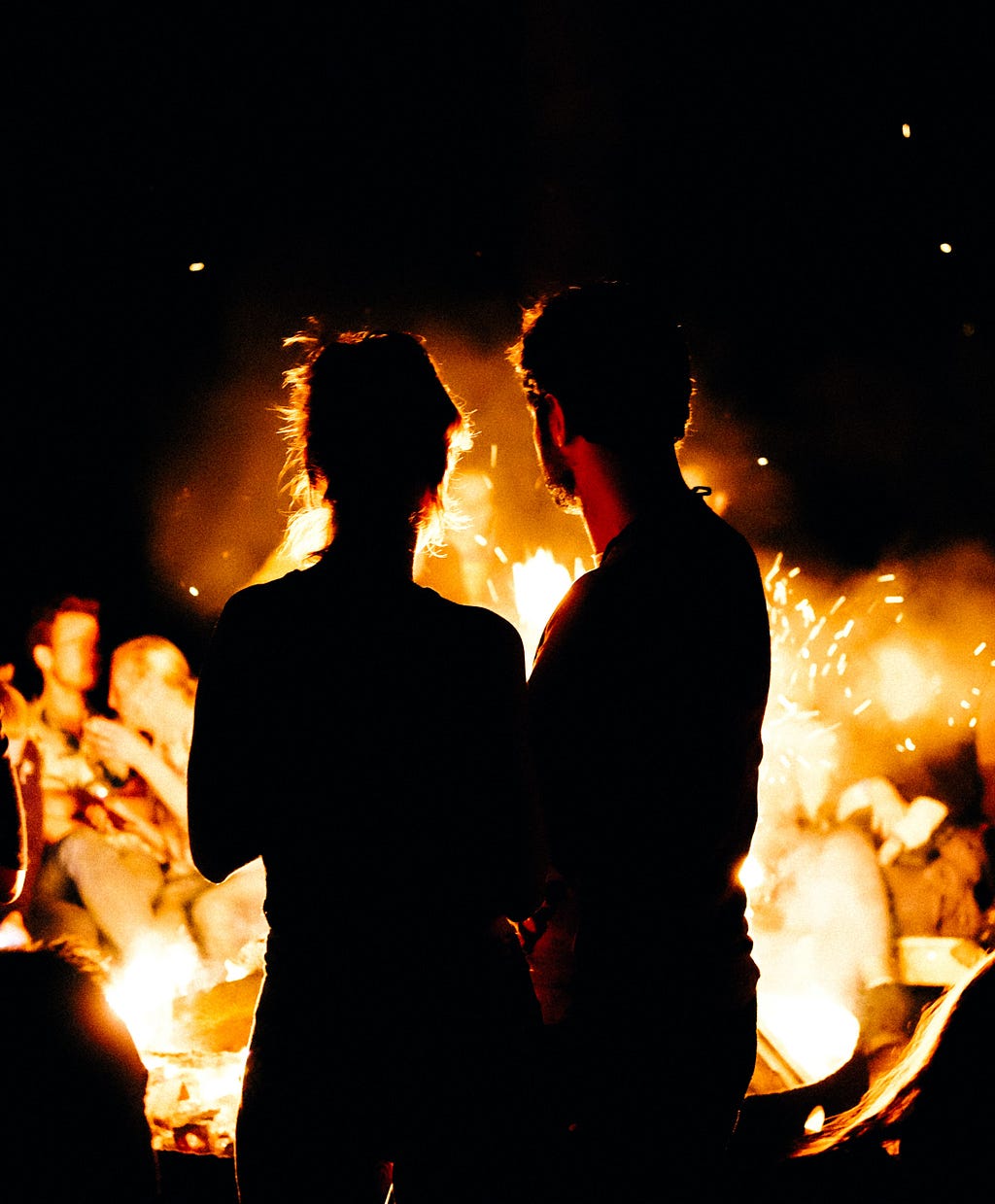 A couple silhouetted by the light of a burning campfire.