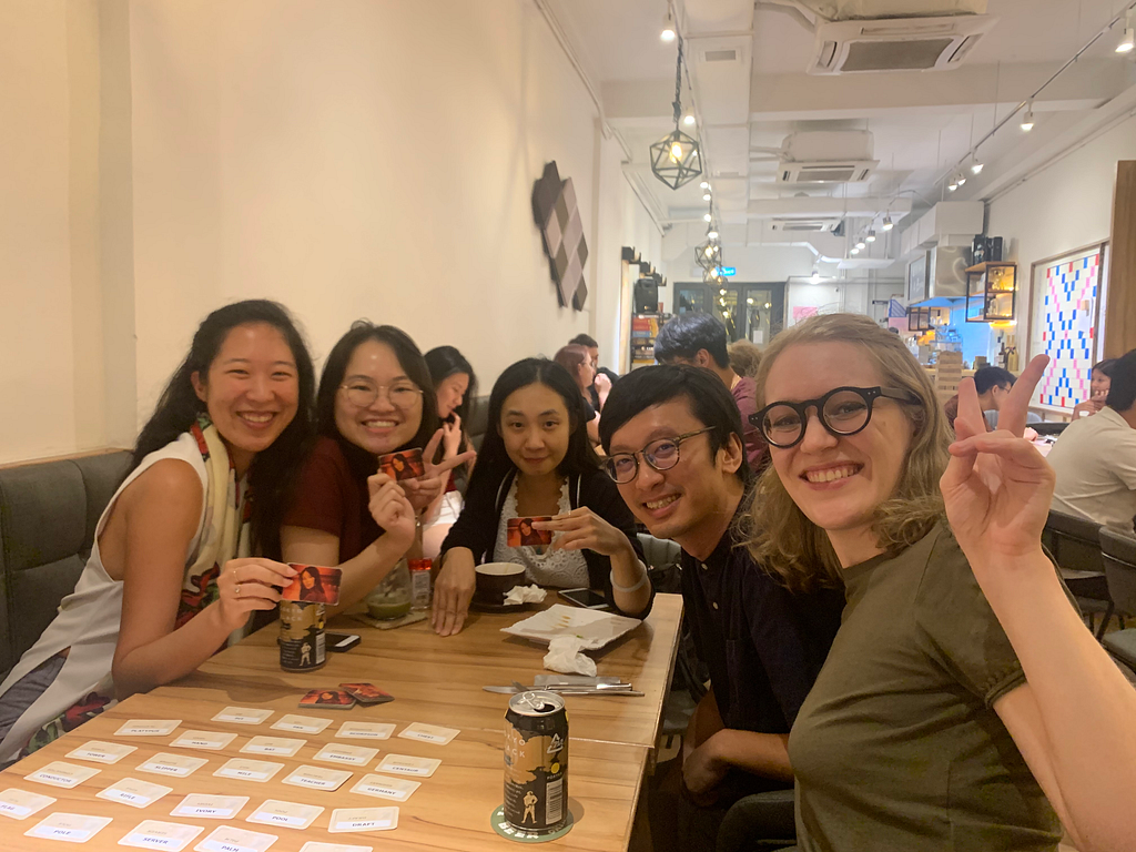 Five people play a card game at a table in a restaurant.