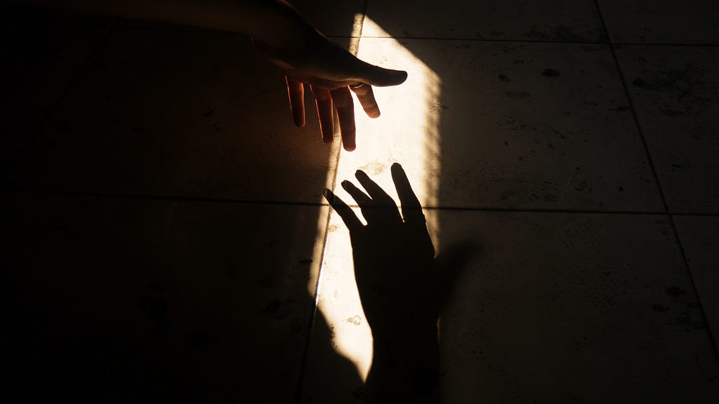 A hand reaching for its shadow in front of a narrow source of light
