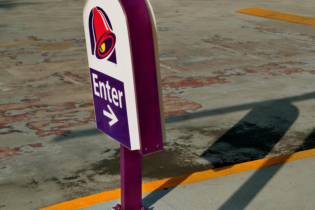 A Taco Bell drive thru sign points to the right with the word “Enter” typed on it.