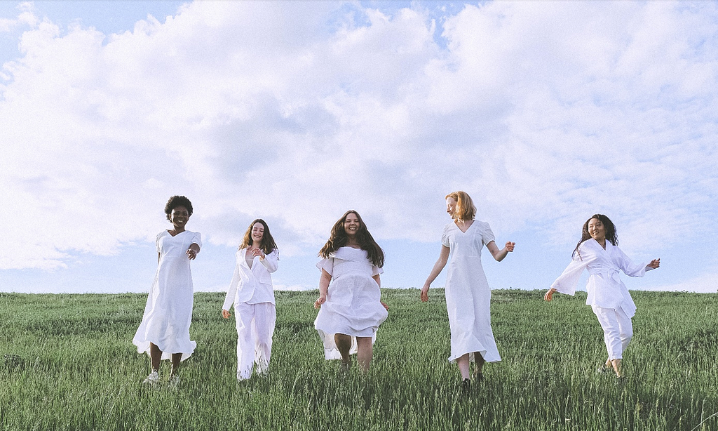 5 women dressed in all white in a field together