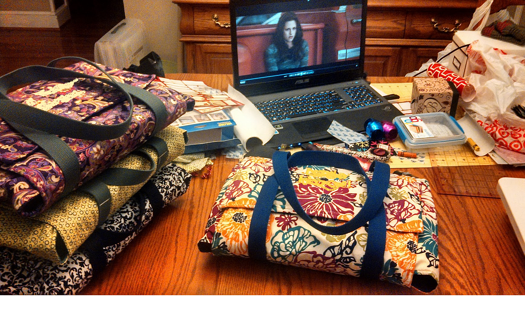 Dining room table with several fabric casserole dish carriers, with a laptop in the background paused on an image of Bella Swan from the first Twilight movie.