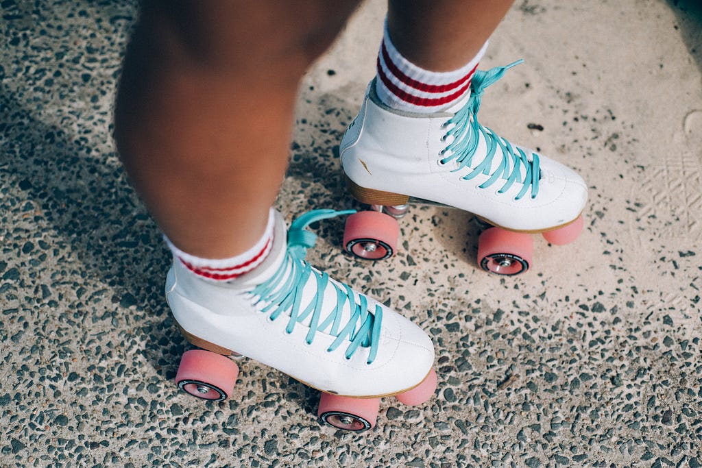 A rollerskater’s legs from the knees down — white roller skates, striped white and red socks, pink wheels.