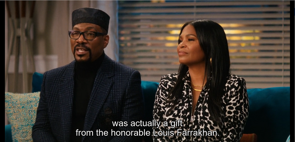 A man with a black Kufi at a dinner table next to a woman. Subtitles read “was actually a gift, from the honorable Luois Farrakhan.”