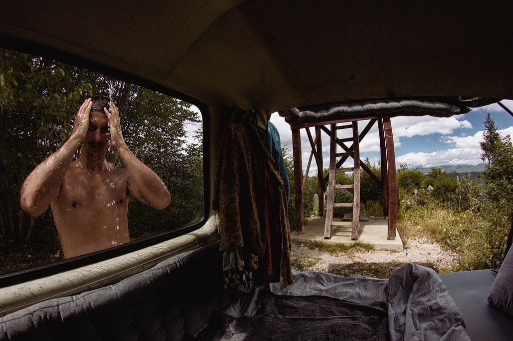 Man showering in nature outside campervan