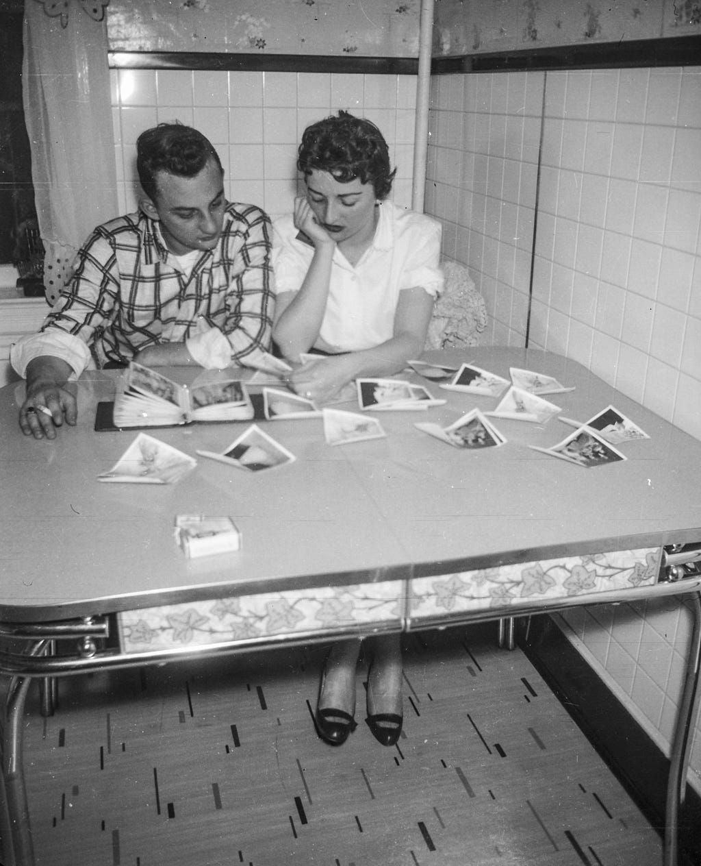 A man and woman sat at an old dining table looking at photographs
