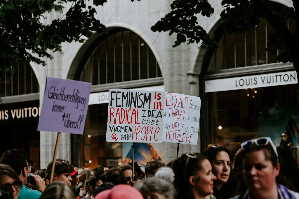 Photo by Claudio Schwarz. A protest by feminists, holding up a sign saying “Feminism is the radical idea that women are people”
