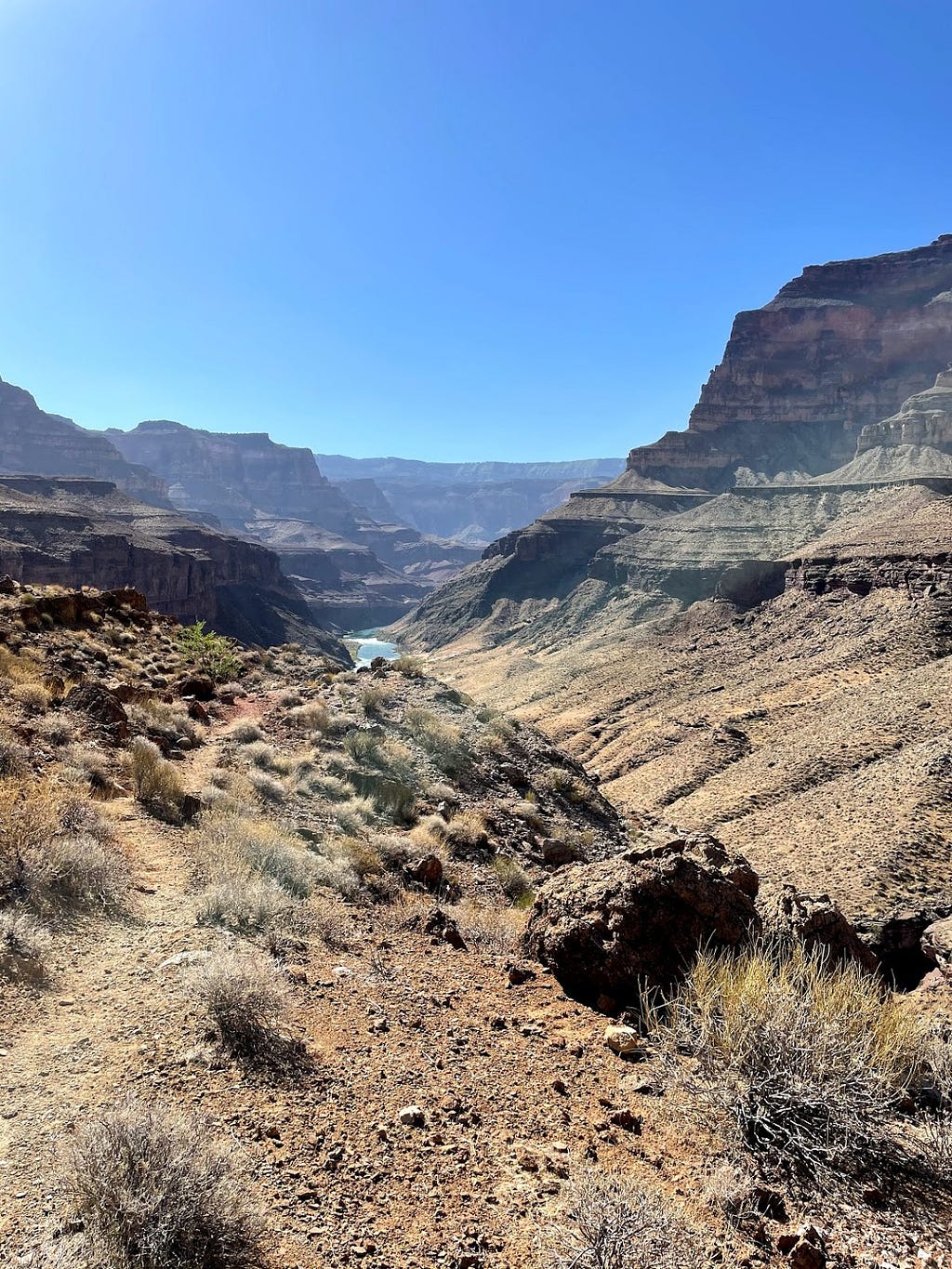 A view of a relatively smooth trail in the grand canyon with a speck of the Colorado River in the distance