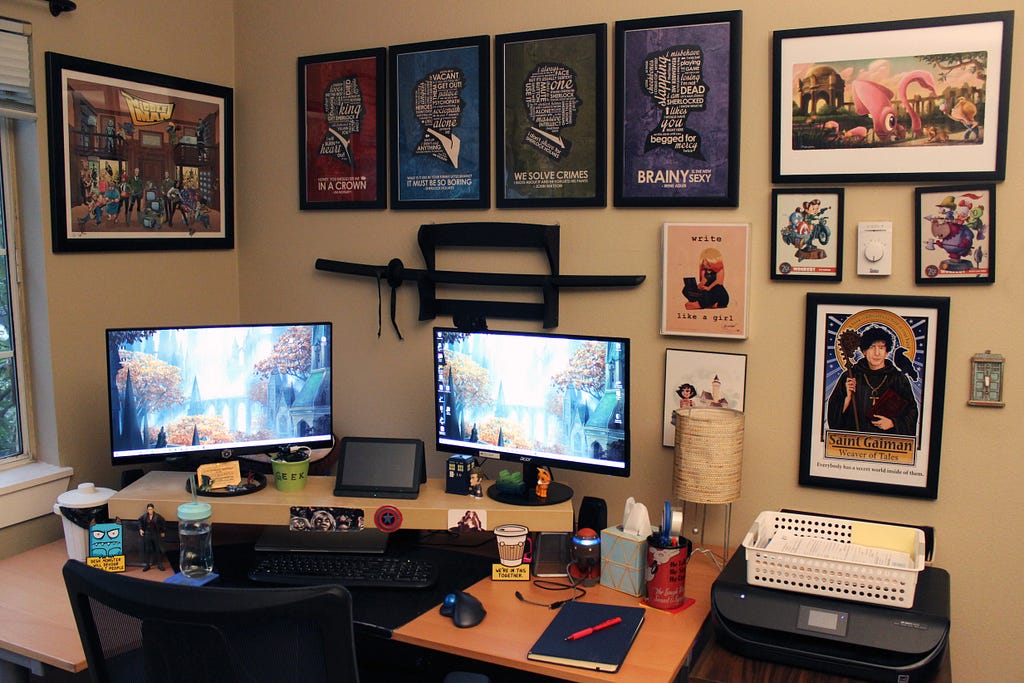 A corner desk with two monitors, artwork on wall, and miscellaneous items on desk