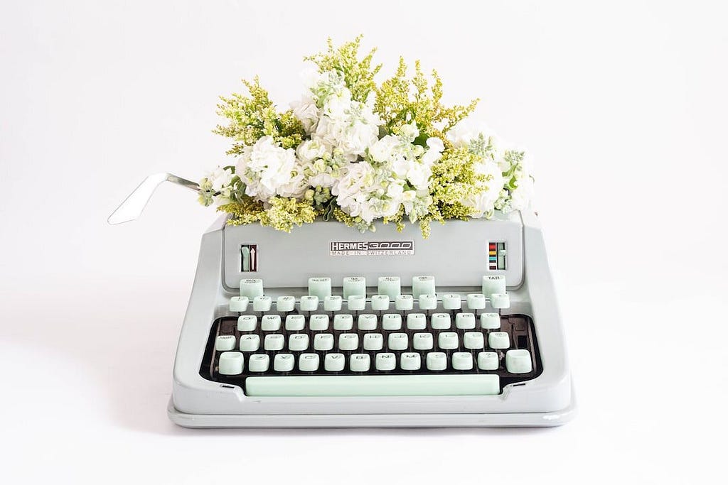 An antique white typewritter topped with white flowers.