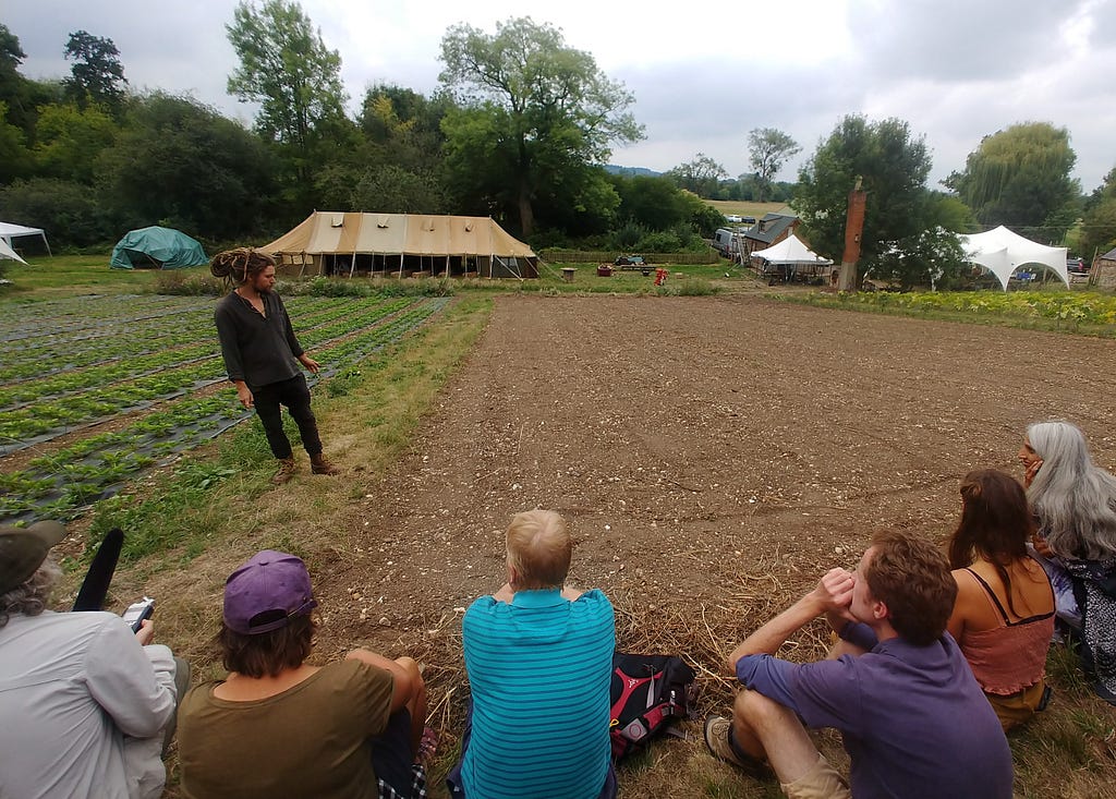 A group of people sit and listen to a man giving a tour of the farm