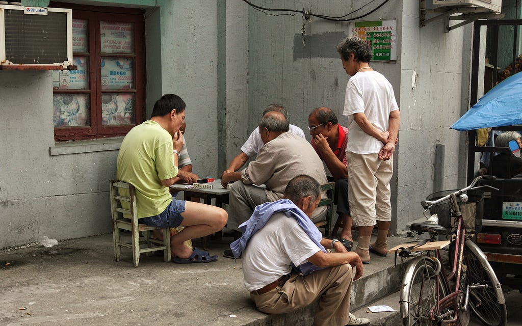 Old men gathering at a table and playing a game.