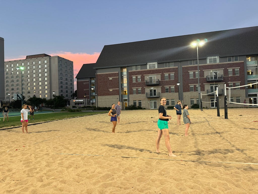 Students play sand volleyball as the sun sets