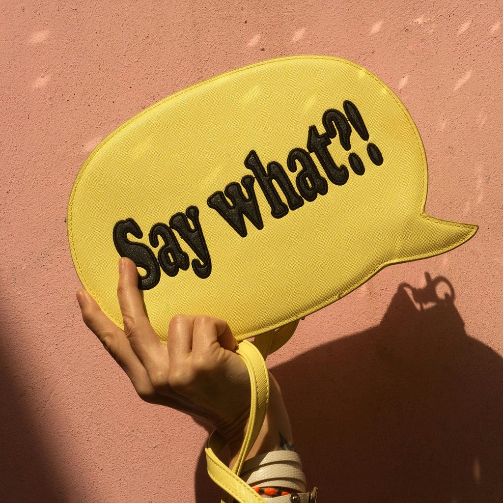 A hand holding up a yellow handbag in the form of a speech bubble, with the text: “Say what?!”