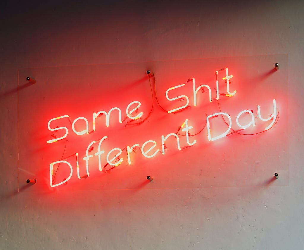 Red neon sign against a white wall that reads, “Same shit different day.”
