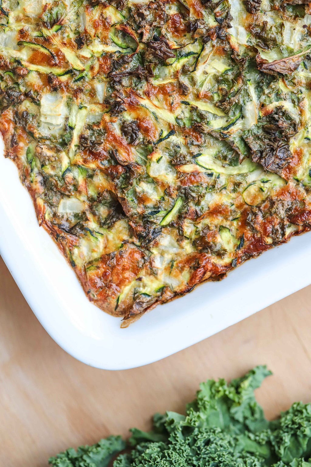 Zucchini and kale breakfast bake in a white baking dish on top of a wooden cutting board