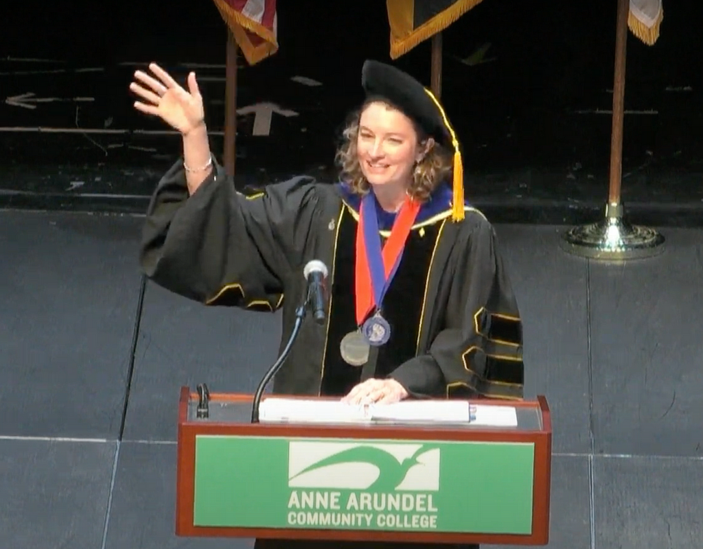 Dr. Hill waves at the crowd from a podium that says Anne Arundel Community College.