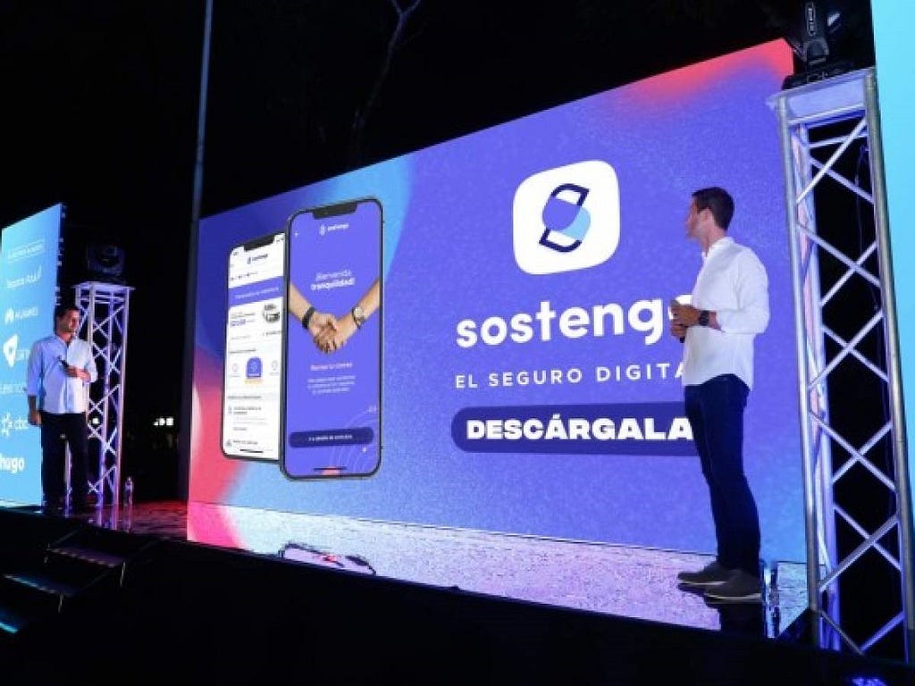 Two men facing each other on a stage, with Sostengo ad in the background.