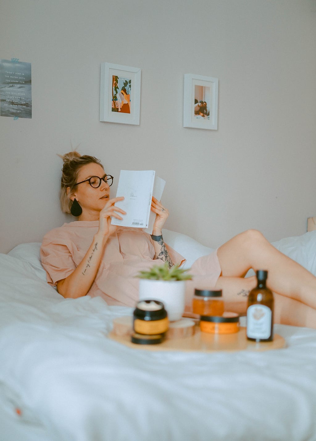 Money mindset: Woman on bed reading book with plant and bottles in front of her