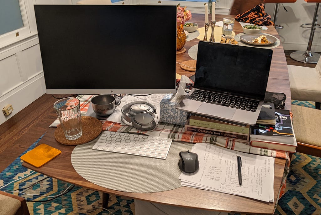 A computer and monitor in a dining room setting with food and candles in the background.
