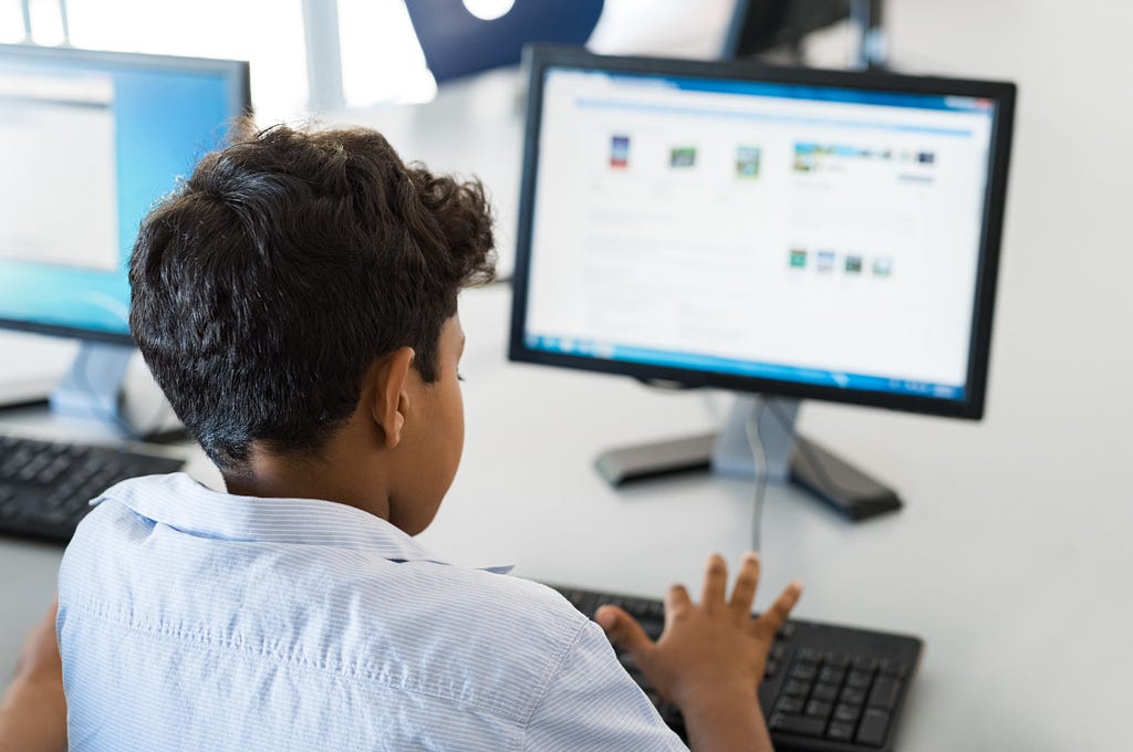 Kid in white shirt working on a desktop.