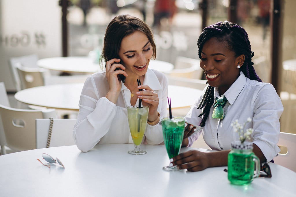 Two ladies in a bar starring at a phone