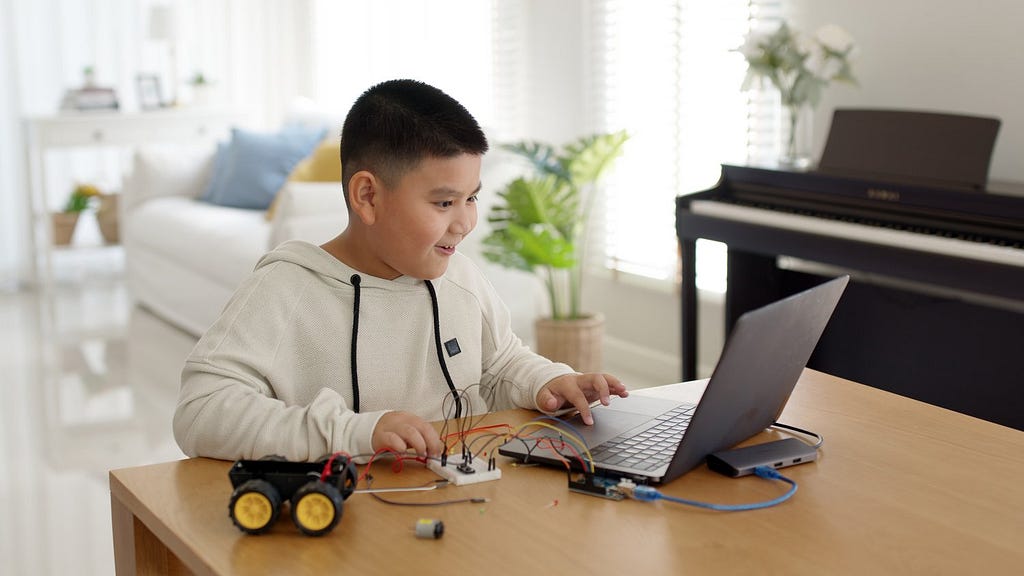Young Asian child creates robotic device by programming arduino device and connecting them to moving parts and power sources.