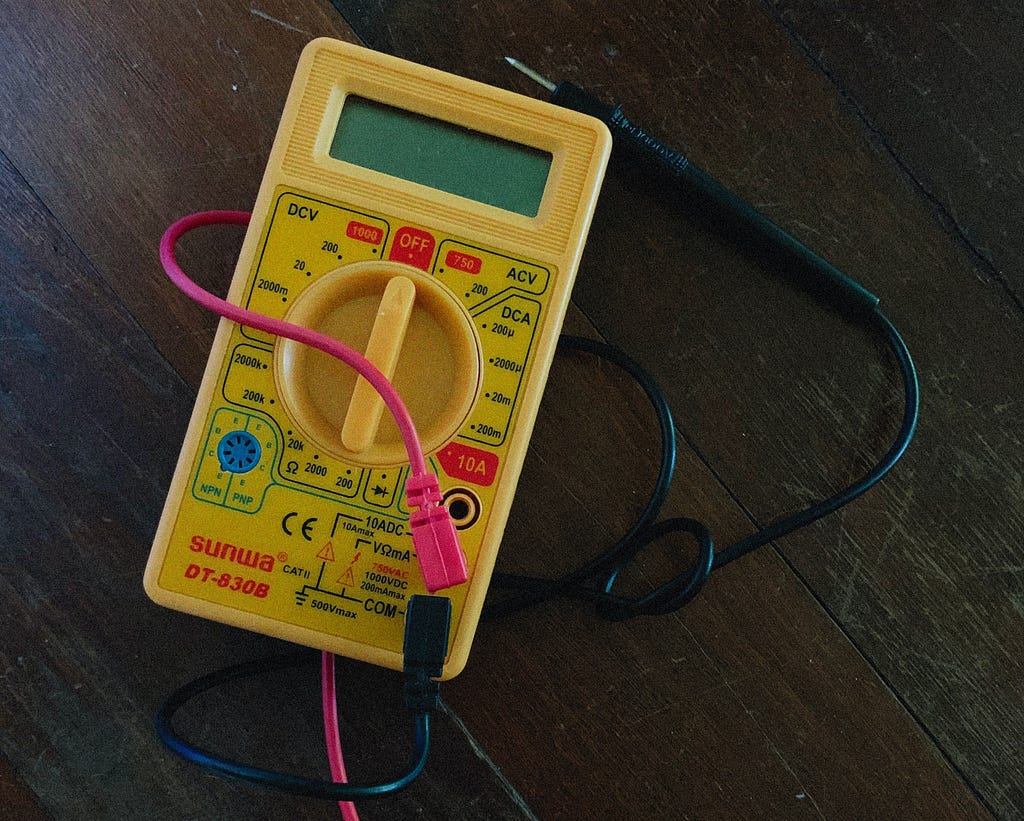 Yellow multimeter with red and black probes laying on a dark wooden table