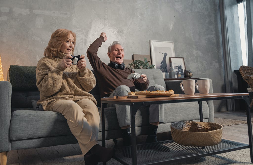 An elderly couple sitting on the sofa and playing video games