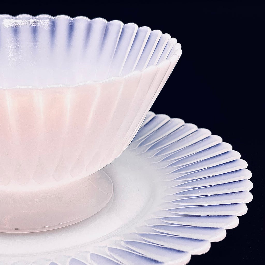 A slant, side view of a Monax Petalware compote dish set atop the matching dessert plate against a black backdrop. The image highlights the diaphanous, lush character of the design.