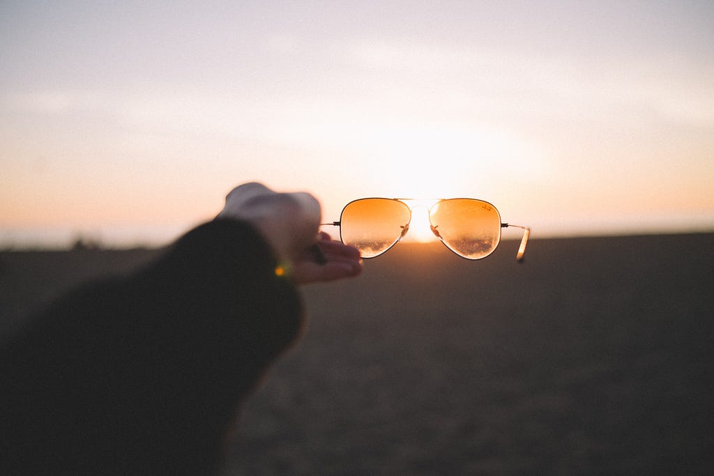 A pair of sunglasses pointing towards the bright setting sun releasing vitamin D.