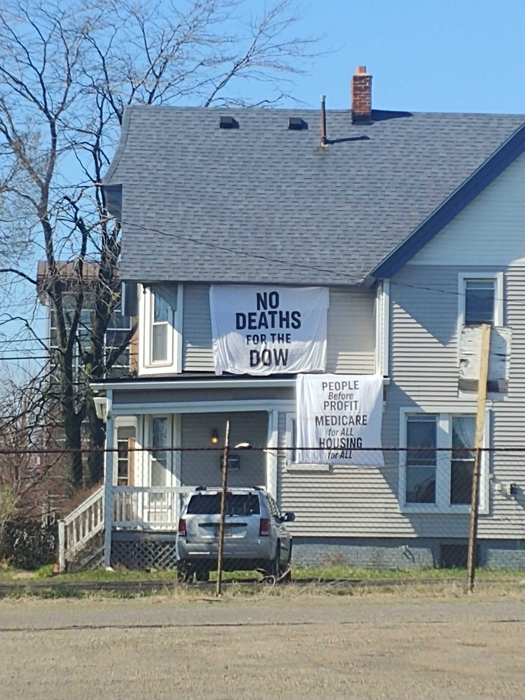 White flags on side of a house read “NO DEATHS FOR THE DOW” and “PEOPLE Before PROFIT MEDICARE for ALL HOUSING for ALL”