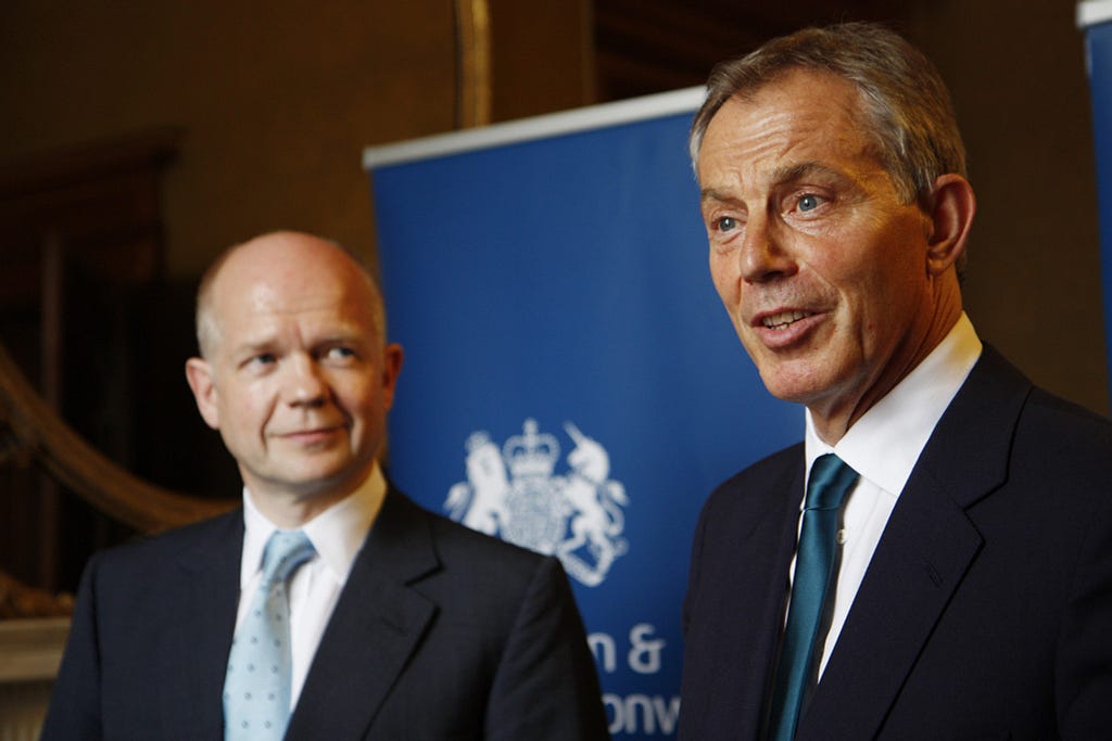 William Hague and Tony Blair in front of a blue government pull-up banner