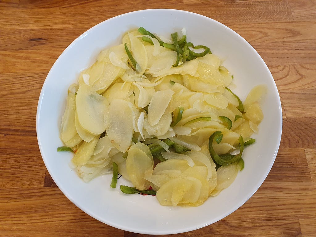 Sliced potatoes, pepper and onion centered in a white bowl against a wooden worktop