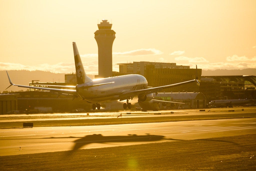 Photo of a passenger aeroplane landing at an airport at sunset, tinting the scene in warm light