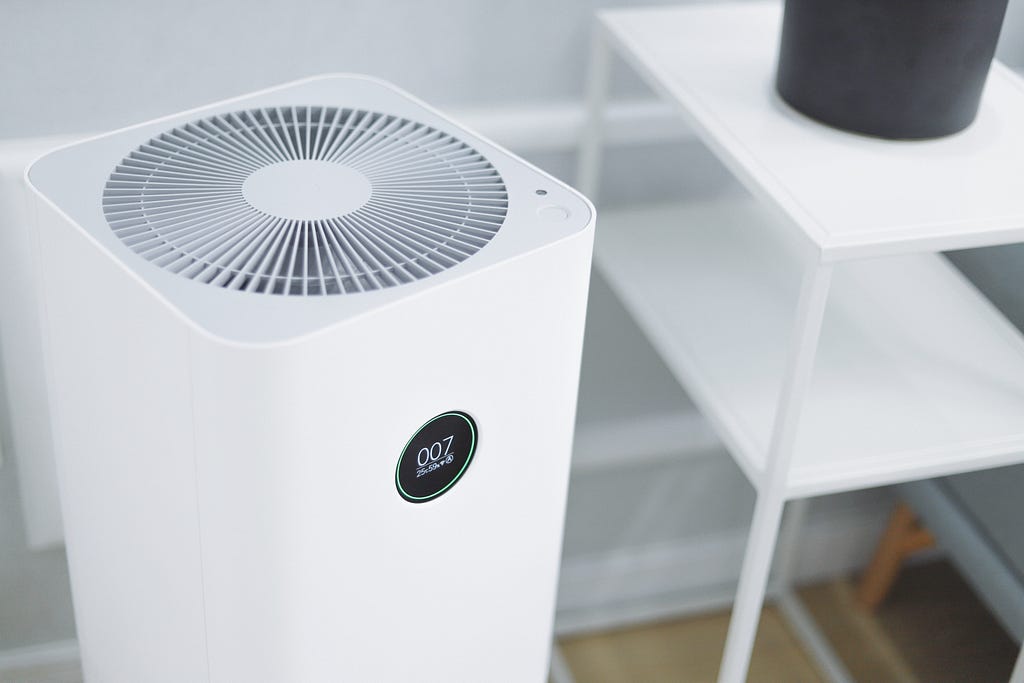 A white, rectangular standing air conditioner next to a small white side table.