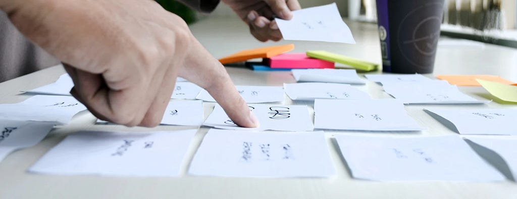 Close of up hand pointing at note cards arranged in a grid on a tabletop.