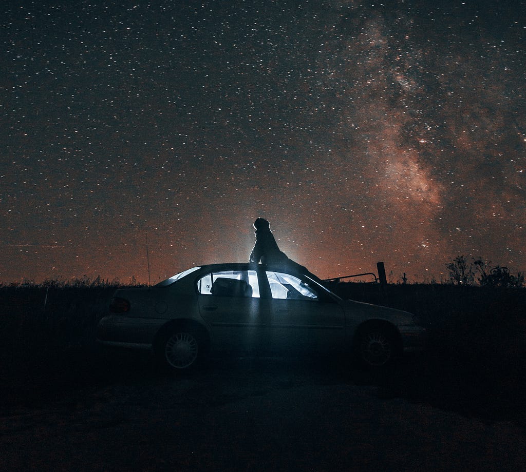 A person sitting on top of a car under a starry night sky