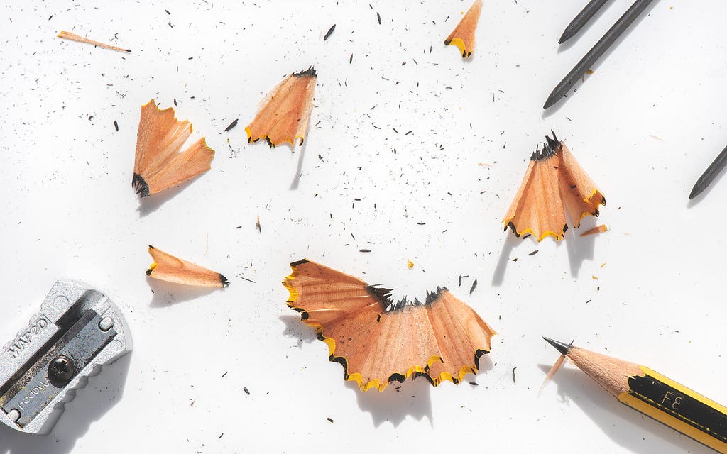 Sharpened pencil with pencil shavings and pencil sharpener on white background.