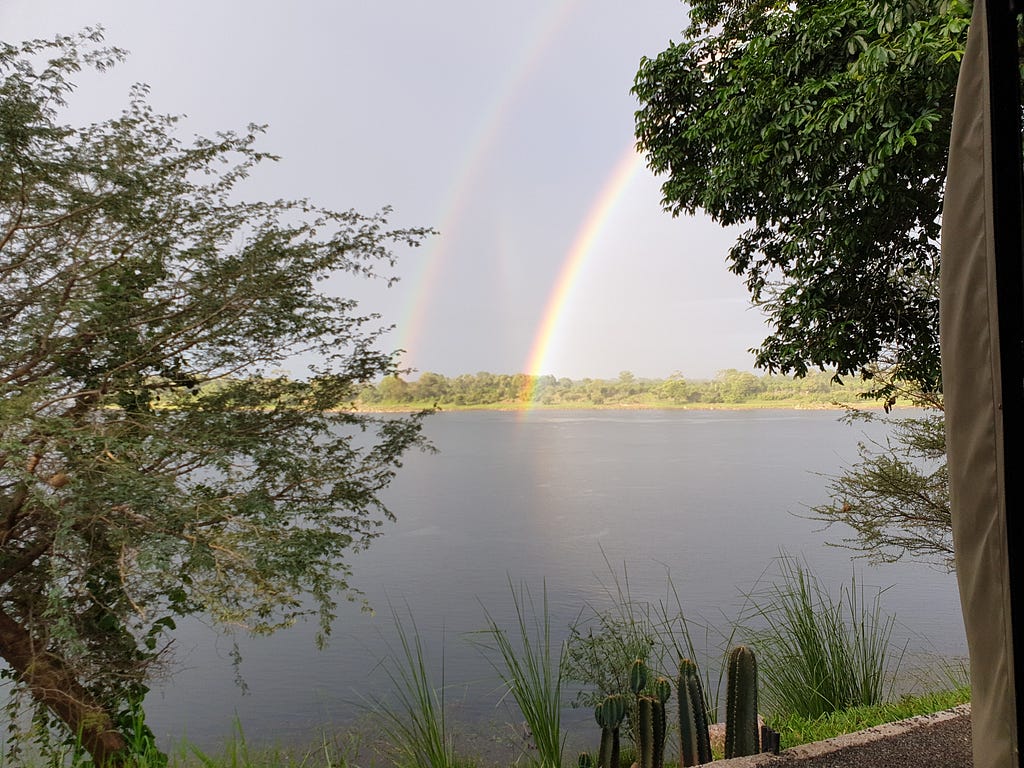A double rainbow curving onto a river, seen between trees