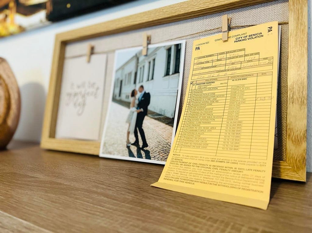 A parking ticket hanging next a photo of a couple on their wedding day, on a shelf.
