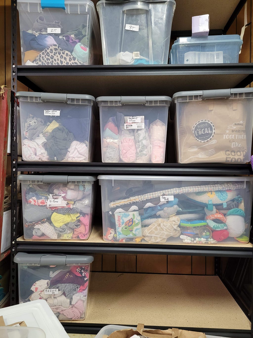 Plastic boxes of baby clothes fill a basement storage rack