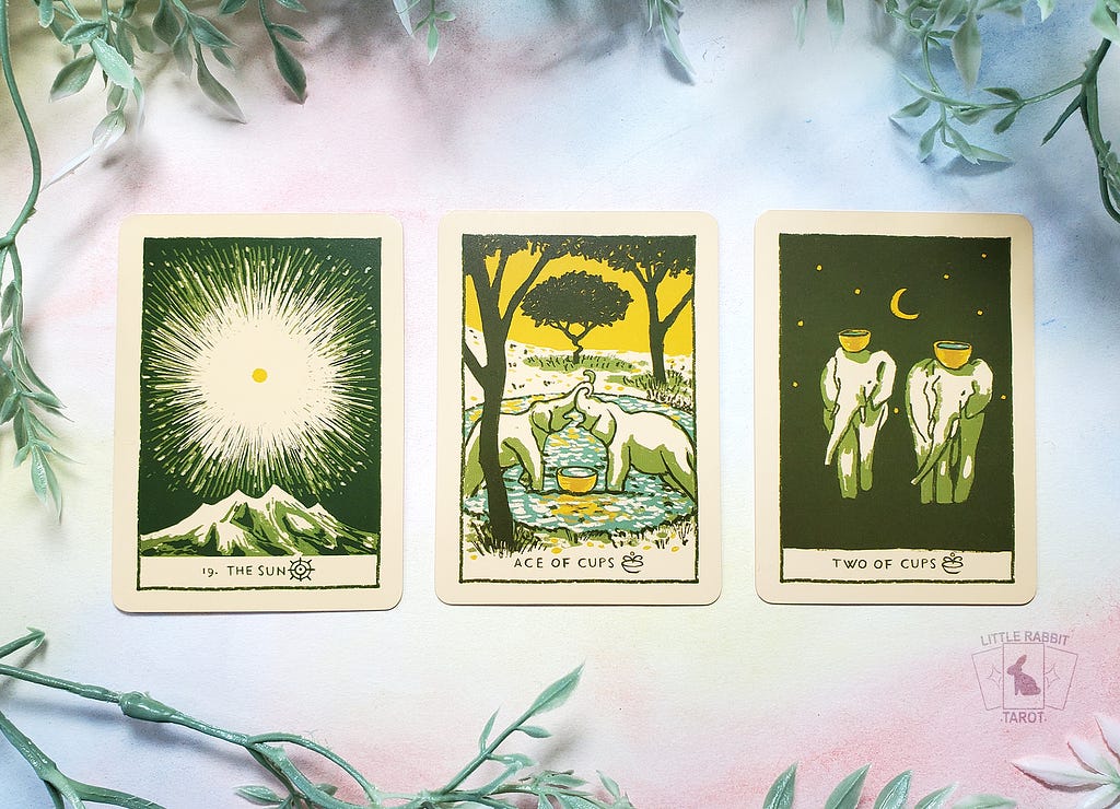A photo of three cards from the Green Glyphs Tarot: The Sun, Ace of Cups, and Two of Cups.