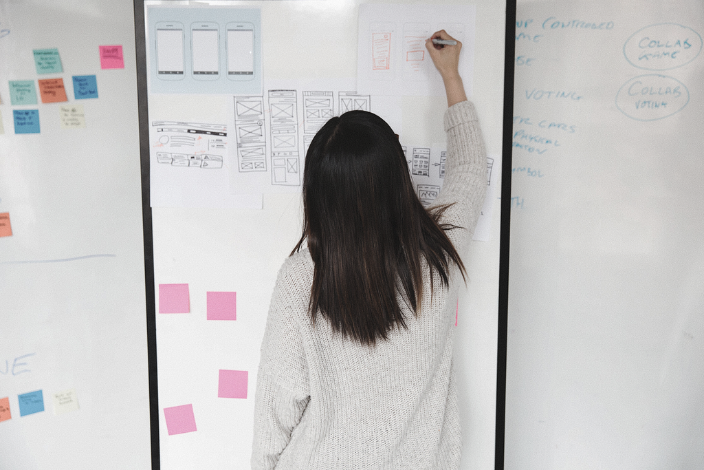 Person standing in front of a whiteboard covered in stickies and drawings, still drawing