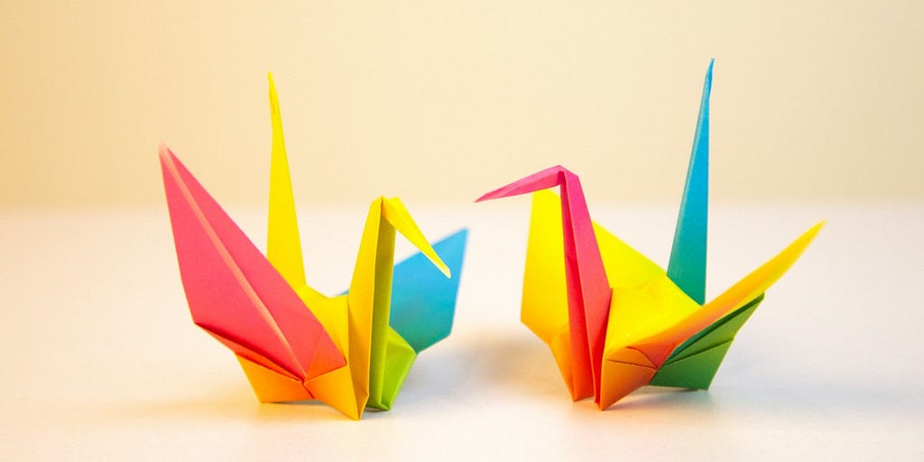 Two multicolored folded paper cranes facing each other.